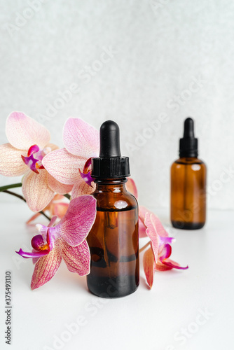 Bottles of essence and surum for skin health on background of flowers. Natural herbal Skin care cosmetics in dark glass. Mockup advertising. Nourishing face oil