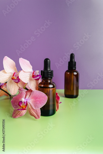 Bottles of essence and surum for skin health on background of flowers. Natural herbal Skin care cosmetics in dark glass. Mockup advertising. Nourishing face oil. Unisex cosmetics. Spa natural 