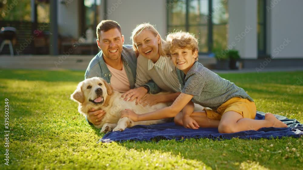 Portrait of Father, Mother, and Son Having Picnic on the Lawn, Posing with Happy Golden Retriever Dog. Idyllic Family Have Fun with Loyal Pedigree Doggy Outdoors in Summer House Backyard. Slow Motion 