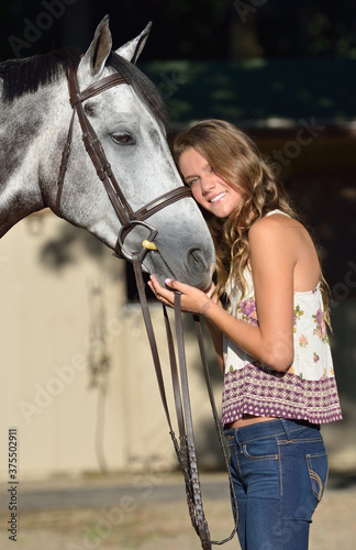 Adorable young girl poses for photo with her horse on a farm in morning sunlight