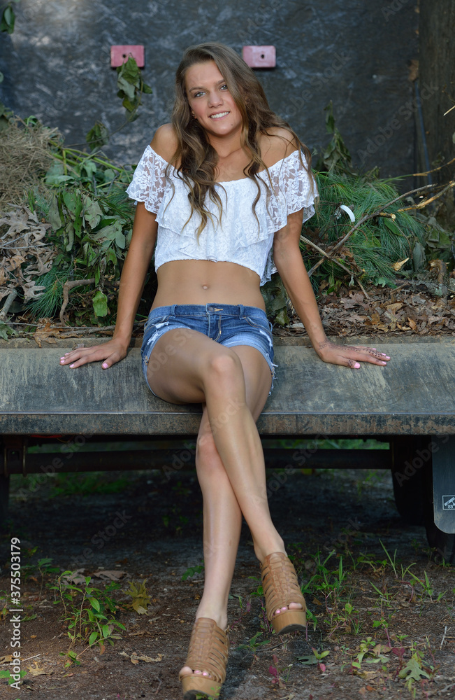 Beautiful girl in white blouse and denim shorts poses on trailer at Beautiful girl in white blouse and denim shorts poses on trailer at