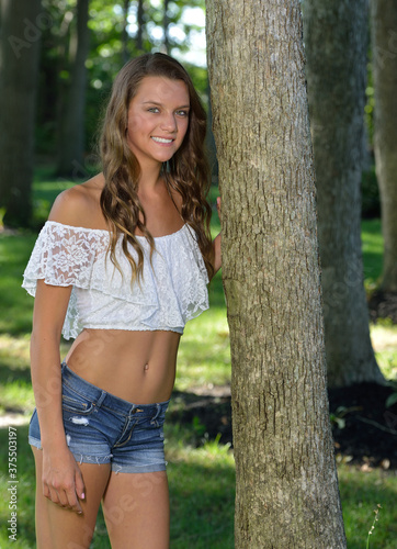 Beautiful girl in white blouse and denim shorts poses onear tree on family farm