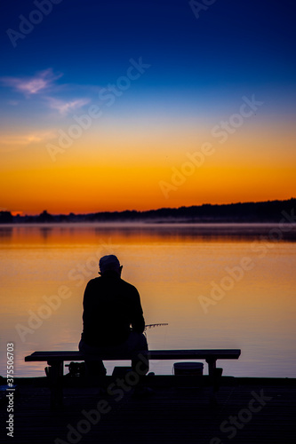 Silhouette of a man sitting near lake fishing at twilight