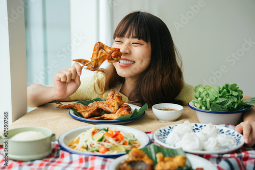 Portrait of young asian woman enjoy eating grilled chicken wing stick.