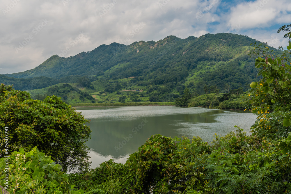 Rural landscape of lake with mountains and cloudy sky in background.