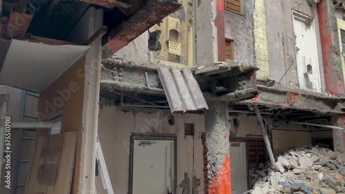 Demolition site of an old house, focusing on a broken girder above then to the rubble on the floor next to an excavator's pincer and bucket.