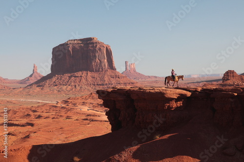 Western Cowboy riding on Horse  from John Ford's Point overlook in Monument Valley Tribal Park with the mittens and Merrick Butte in Arizona, USA