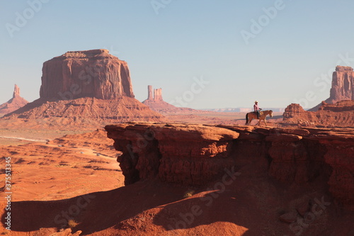Western Cowboy riding on Horse from John Ford's Point overlook in Monument Valley Tribal Park with the mittens and Merrick Butte in Arizona, USA