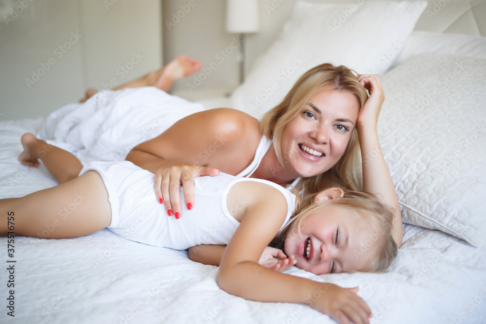 young woman hugging with her daughter on a white bed young woman hugging with her daughter on a white bed