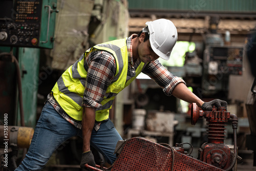 Portrait of young handsome technician man or industrial worker with hard hat or helmet and vest jacket working electronic machinery and mechanical engineering in Factory of manufacturing place