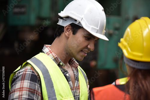 Portrait of young handsome technician man or industrial worker with hard hat or helmet and vest jacket working electronic machinery and mechanical engineering in Factory of manufacturing place photo