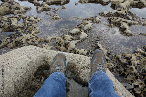 Grautönige Steinformation mit Wasserpfützen und zwei neutralen Füßen in braunen Wanderschuhen.