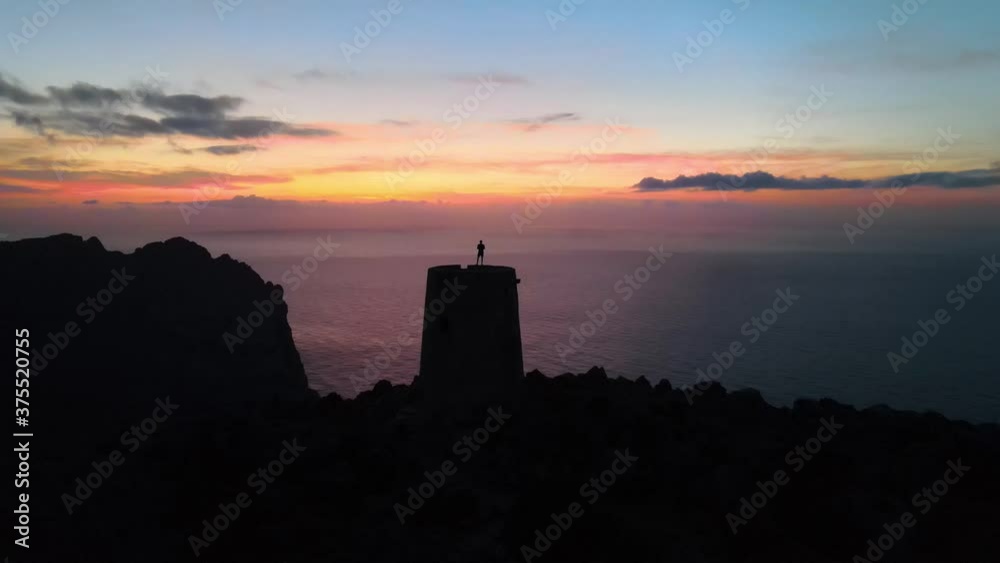 Aerial shot flying over the silhouette of a man standing on top of a watchtower on a spectacular sunset Aerial shot flying over the silhouette of a man standing on top of a watchtower on a spectacular sunset