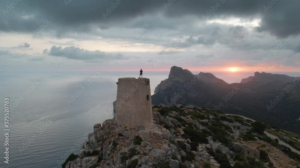 Aerial shot of a man standing on top of an old watchtower with an incredible sunset on background Aerial shot of a man standing on top of an old watchtower with an incredible sunset on background