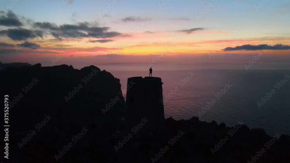 Aerial silhouette shot of a man standing on top of an old watchtower at the coast. Orbiting shot Aerial silhouette shot of a man standing on top of an old watchtower at the coast. Orbiting shot