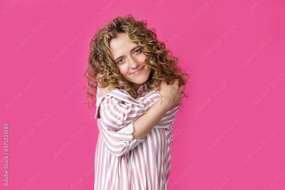 Waiting for a special moment. Portrait of a smiling woman who hugs herself with her arms. Isolated on a pink background Waiting for a special moment. Portrait of a smiling woman who hugs herself with her arms. Isolated on a pink background