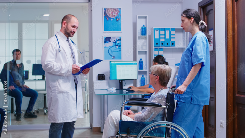 Doctor checking diagnosis of disabled senior woman in wheelchair. Medical staff in hospital hallway with invalid patient. Man in medical examination room. Doctor checking diagnosis of disabled senior woman in wheelchair. Medical staff in hospital hallway with invalid patient. Man in medical examination room.