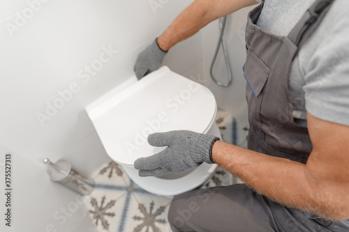 Fotografie Plumber in medical mask installing toilet bowl in restroom, work in bathroom