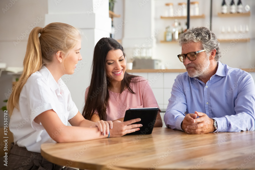 Female agent or manager meeting with couple of young and mature customers, presenting content on tablet. Man and woman looking at screen, smiling, laughing. Consulting or technology concept Female agent or manager meeting with couple of young and mature customers, presenting content on tablet. Man and woman looking at screen, smiling, laughing. Consulting or technology concept