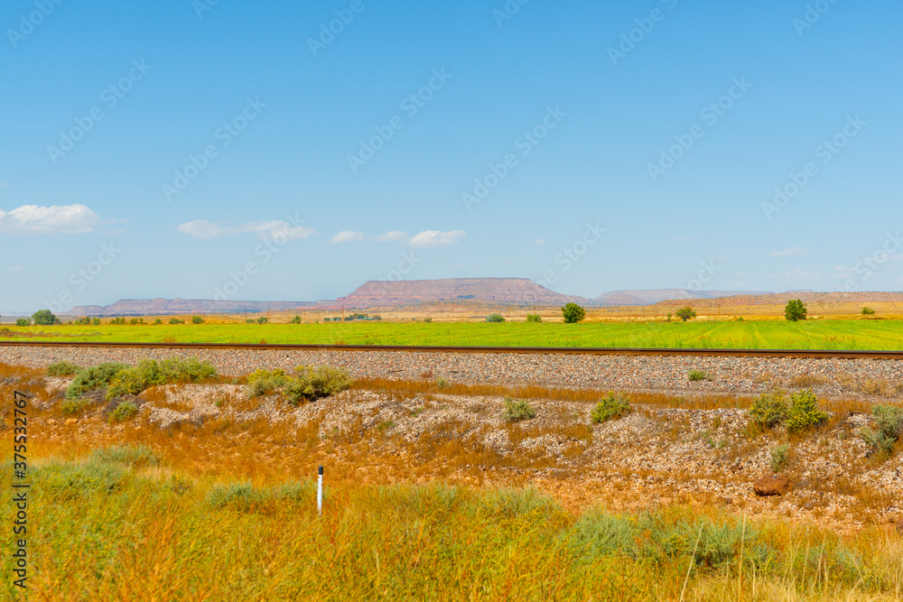 Fototapeta premium Flat plains of New Mexico with distant flat-top mesa landform in distance and railway tracks through foreground.