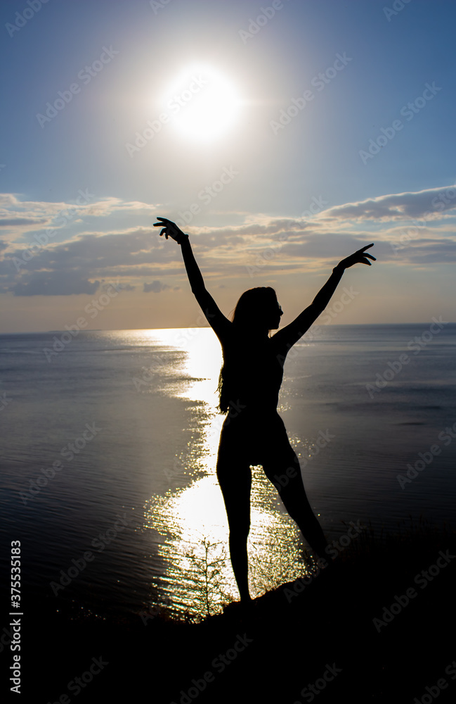 silhouette of a beautiful slender dancing girl on the background of the sea and sunset
