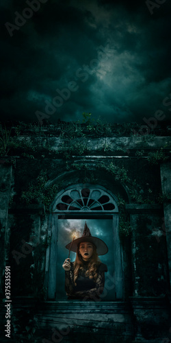 Halloween witch holding magic wand standing over ancient castle window  full moon with spooky cloudy sky  Halloween mystery concept