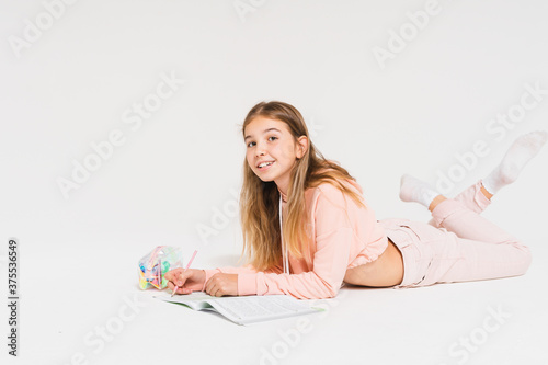Tableau sur toile Cute smiling teen girl with long hair in pink hoodie doing homework isolated on