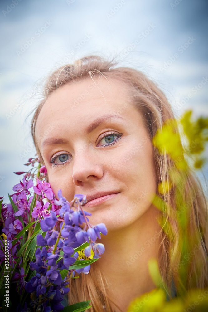 Portrait of beautiful blonde girl in field with a bouquet of flowers on a cloudy summer day Portrait of beautiful blonde girl in field with a bouquet of flowers on a cloudy summer day