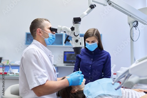 Male doctor dentist treating teeth using dental microscope instruments