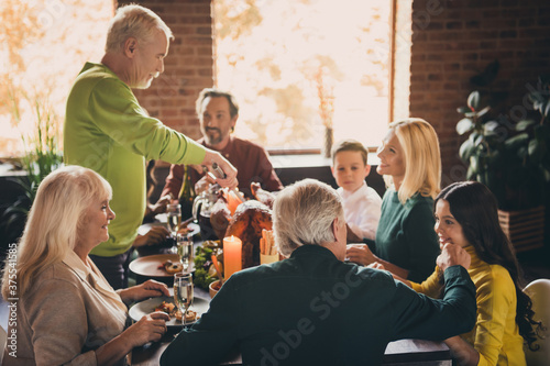 Portrait of nice attractive careful foster adopted cheerful family sitting around served table cutting domestic turkey harvest autumn November at modern loft industrial brick interior house