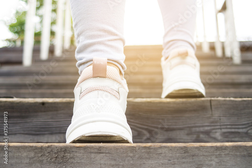 Female legs shod in sport sneakers on the wooden stairs