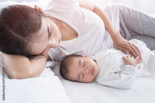 Loving mom carying of her newborn baby at home. Bright portrait of happy mum holding sleeping infant child on hands. Mother hugging her little. Mother and her baby son, sleeping on a big bed.