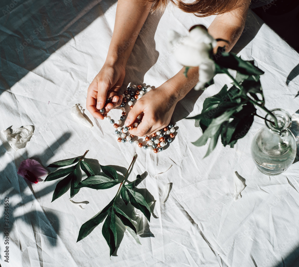 child's hands hold jewelry. girl holding multi-colored beads in her hands. decorations on a white table covered with a white tablecloth. decorations on a table bathed in the sun. decorations and flowe child's hands hold jewelry. girl holding multi-colored beads in her hands. decorations on a white table covered with a white tablecloth. decorations on a table bathed in the sun. decorations and flowe