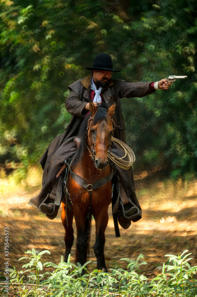 The cowboy is on the horse, standing in the forest and holding a gun. The cowboy is on the horse, standing in the forest and holding a gun.