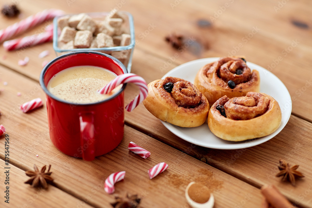 christmas and seasonal drinks concept - eggnog in red cup with candy cane decoration, cinnamon buns and aromatic spices on wooden background christmas and seasonal drinks concept - eggnog in red cup with candy cane decoration, cinnamon buns and aromatic spices on wooden background