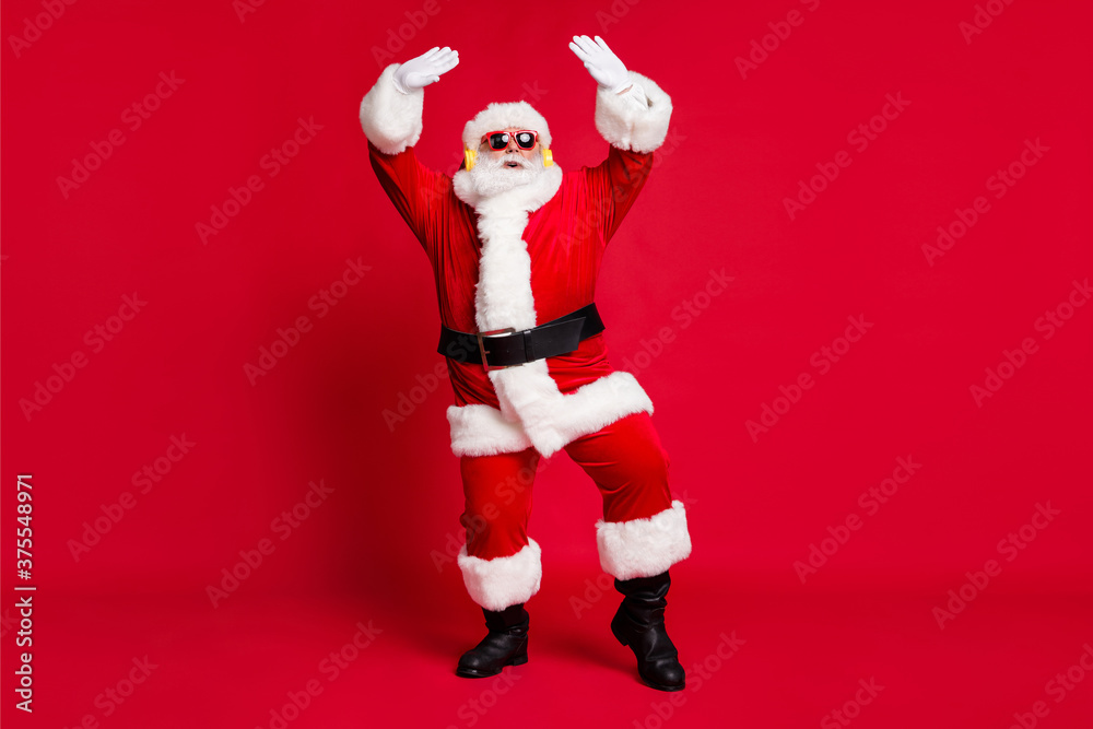 Full body size photo of pensioner old man grey beard hands up party good time wear santa costume x-mas coat belt sunglass headwear earphones black boots isolated red color background