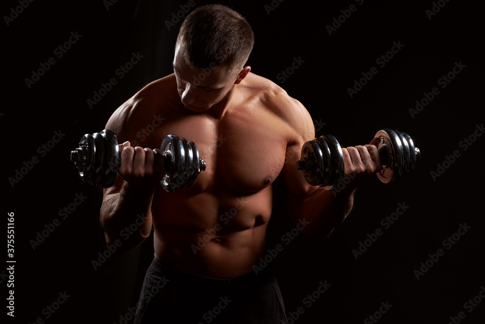 Shirtless muscular man holding dumbbells against of black background.Studio shot