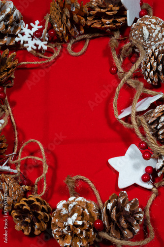 red christmas background with a frame of many pine nuts and stars tied to a rope and space to add text