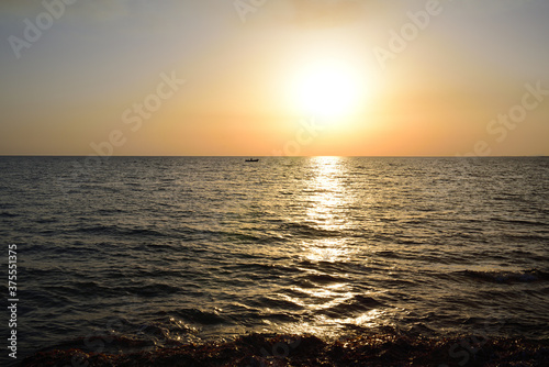 In the evening at sunset, a lonely fishing boat floats on the sea, with gentle waves lapping against the shore