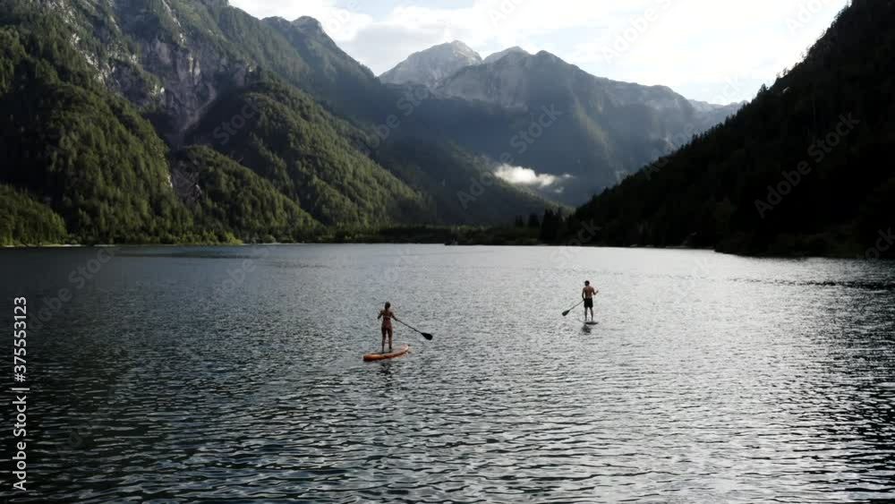 Stand up paddle with a view, woman and man on SUP in the mountains looking at forest and mountain range. Couple enjoying outdoor activities on alpine lake. Stand up paddle with a view, woman and man on SUP in the mountains looking at forest and mountain range. Couple enjoying outdoor activities on alpine lake.