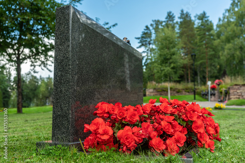 Single black gravestone with red flowers on a beautiful and well cared cemete...