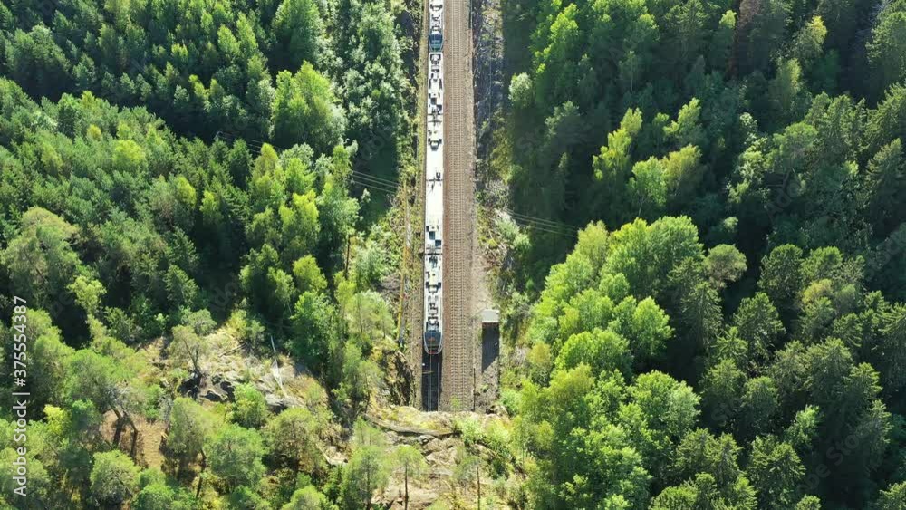Aerial view of the high-speed commuter train moves on the railroad in the countryside in Espoo, Finland. The railroad between the hills goes into a tunnel.