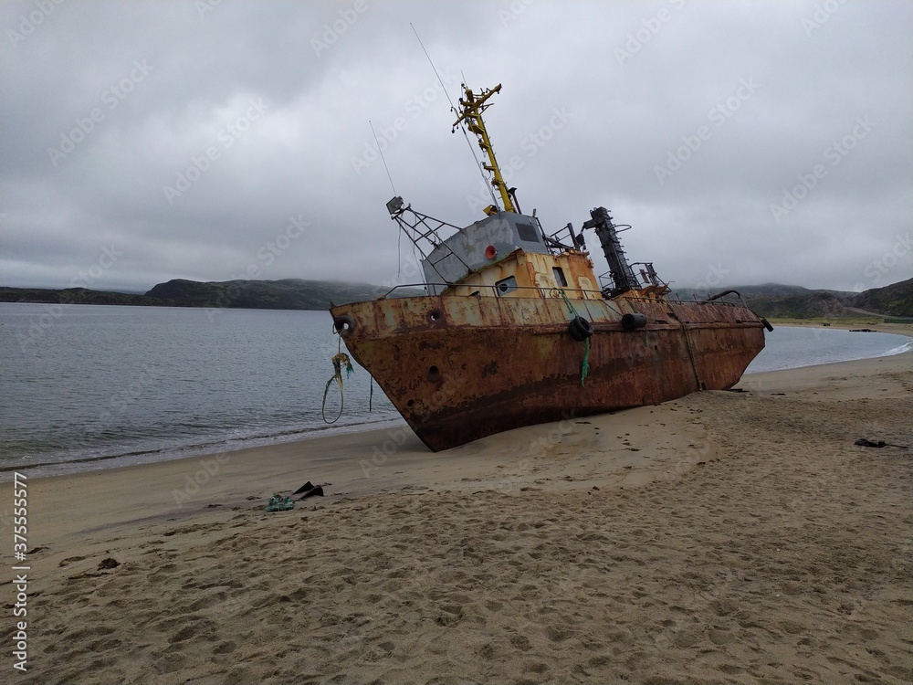 Old abandoned rusty metal ship on the sandy shore of the barents sea