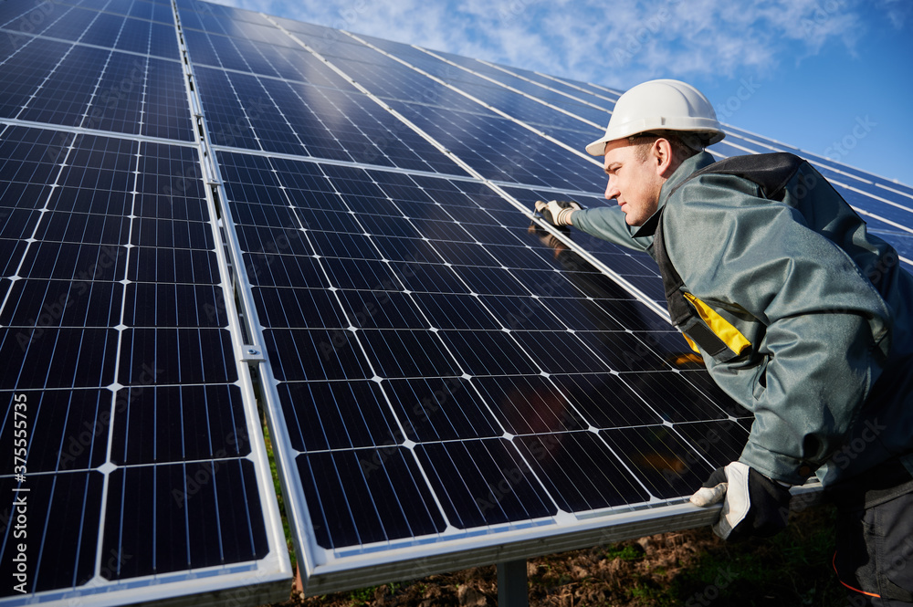 Professional worker, wearing protective suit, helmet and gloves, installing a photovoltaic solar batteries on a sunny day. Concept of alternative energy and power sustainable resources. Professional worker, wearing protective suit, helmet and gloves, installing a photovoltaic solar batteries on a sunny day. Concept of alternative energy and power sustainable resources.