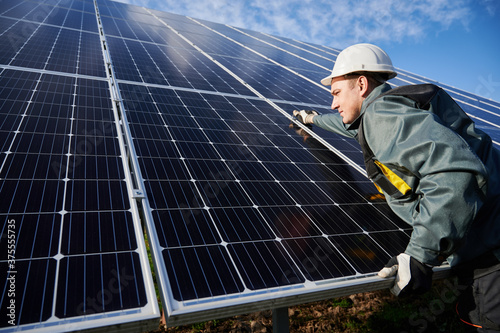 Professional worker, wearing protective suit, helmet and gloves, installing a photovoltaic solar batteries on a sunny day. Concept of alternative energy and power sustainable resources.