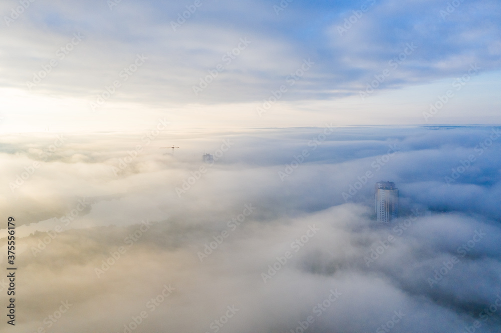 Photo from a height of a foggy city! Several buildings and a construction crane can be seen through the fog.