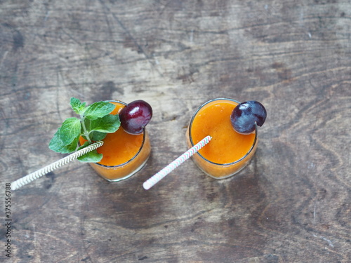 Natural products idea. Glass of plum juice or smoothie with paper straw on wooden natural table with fresh plums.