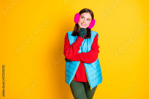 Photo of minded interested girl touch green mittens chin look copyspace think thoughts decide winter holidays wear blue pink trousers pants isolated over bright shine color background