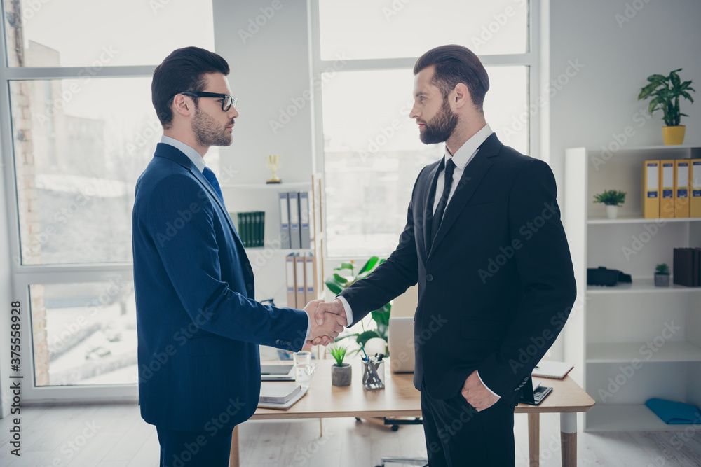 Profile side view of two nice attractive content trendy imposing men qualified finance expert employer hr shaking hands hiring talent human resources at light white interior workplace workstation