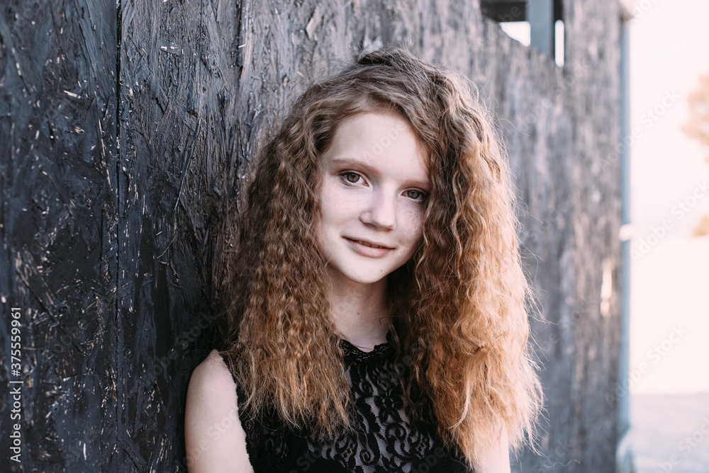 Fototapeta premium Red-haired girl in a black dress near a dark textured wall
